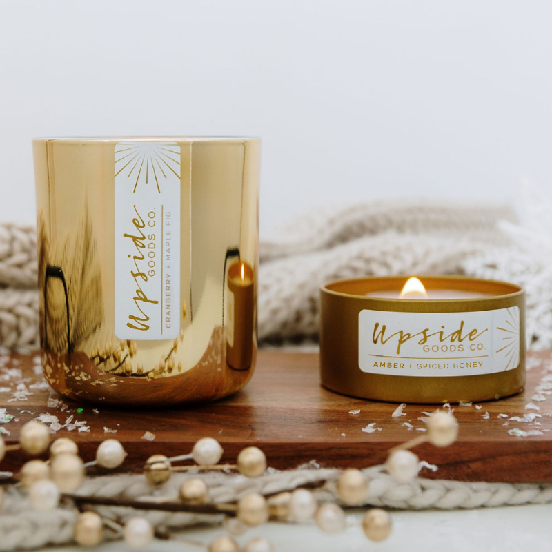 Gold candle with 'Upside Goods Co' label on a wooden surface with decorative elements.