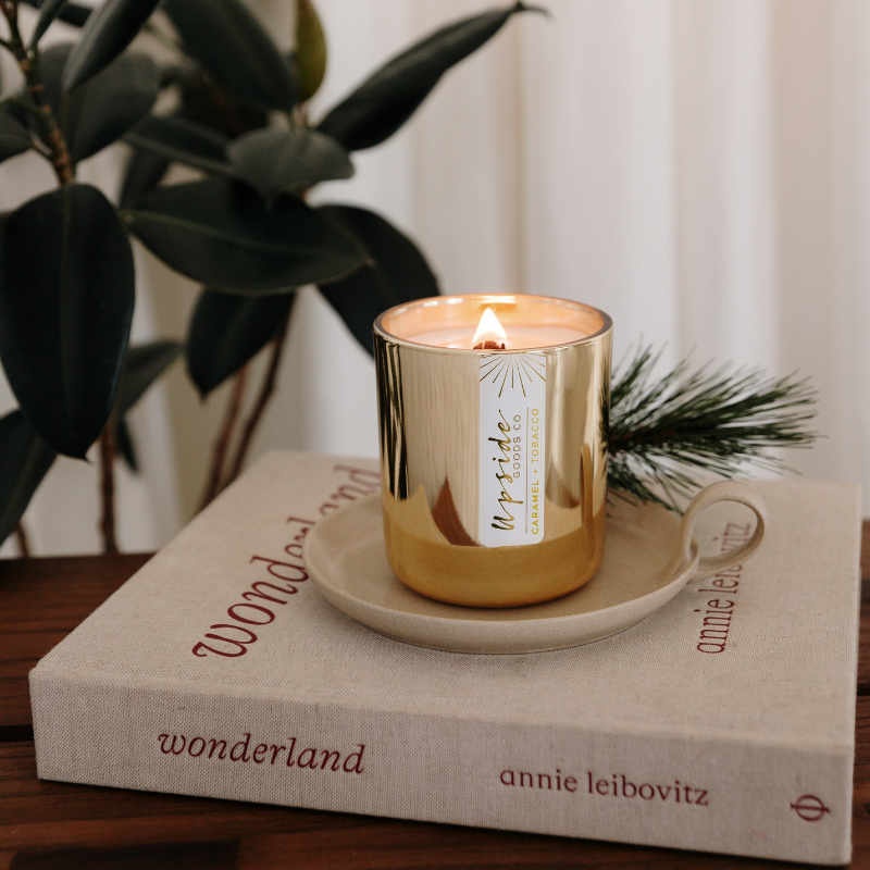 Gold candle on a book with a plant in the background, limited edition from Upside Goods Co. Holiday Collection