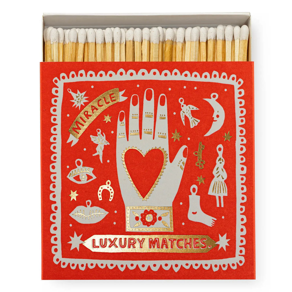Matchbox with decorative design featuring a hand holding a heart and various symbols on a red background.