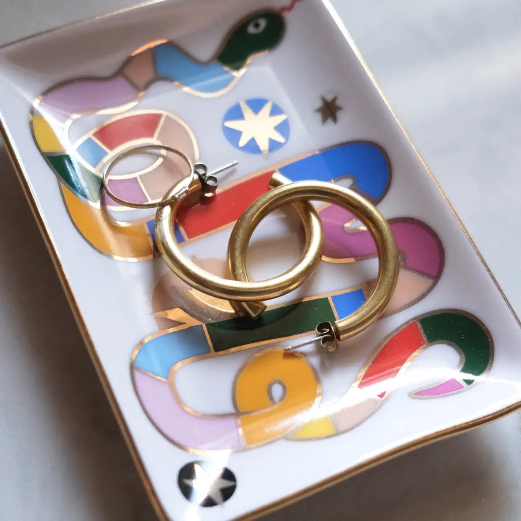 Gold hoop earrings on a colorful abstract-patterned dish